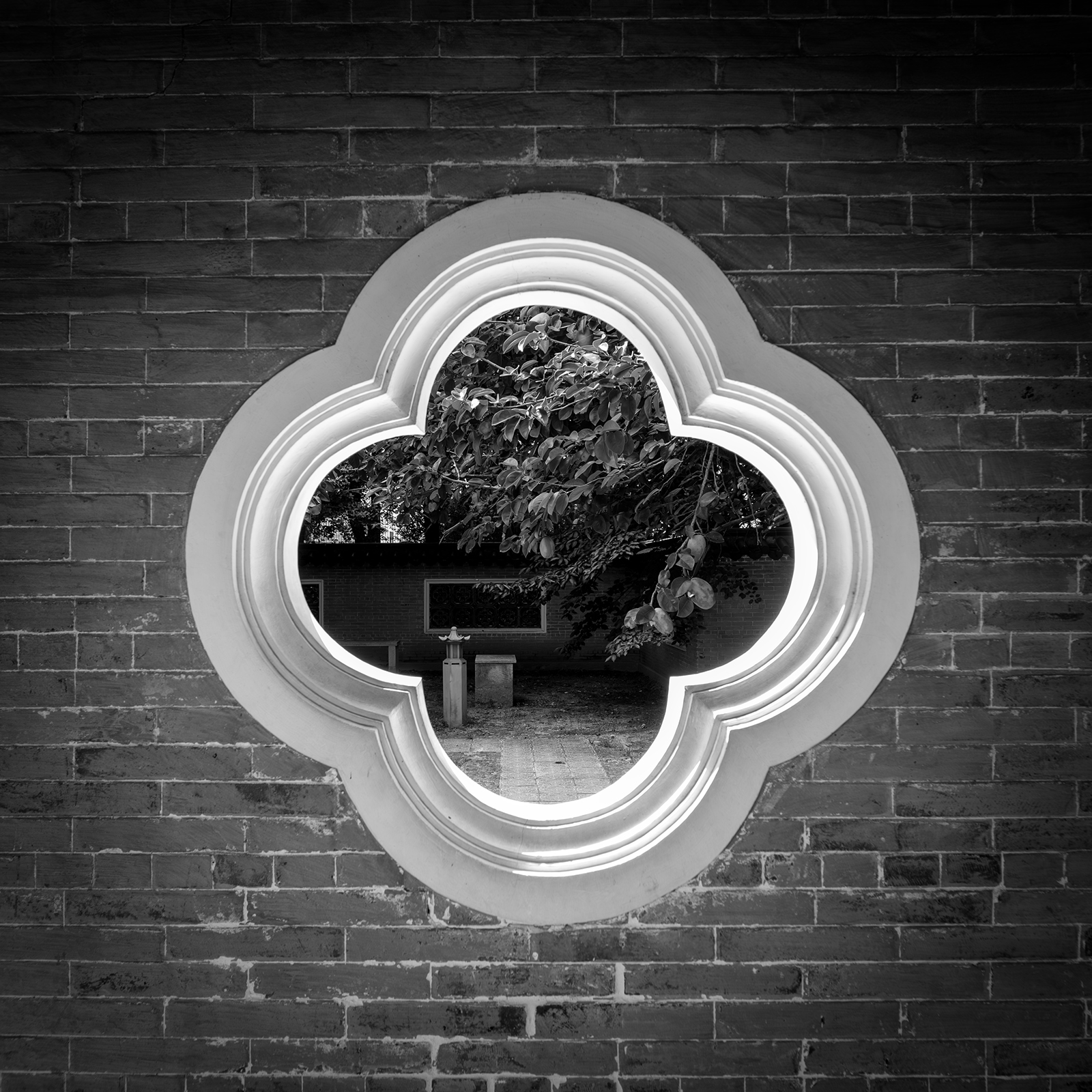 Wolhwawon - A black-and-white view frames leafy garden details through a bright quatrefoil window set in a dark brick wall. - #Wolhwawon #WolhwawonGarden #Suwon #SuwonKorea #HyowonPark #GyeonggiDo #SouthKorea #KoreaTravel #VisitKorea #TravelKorea