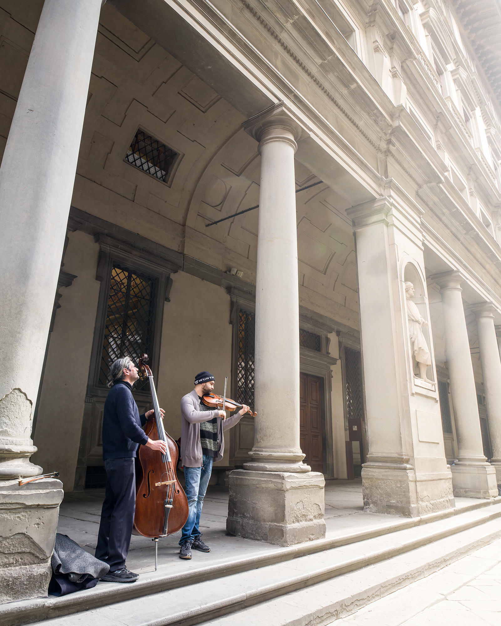 Busking - Two street musicians play double bass and violin beneath a grand colonnade in soft daylight. - #Florence #Firenze #FlorenceItaly #Busking #BuskingInFlorence #StreetMusic #StreetMusician #StreetPerformance #StreetArtist #LiveMusic