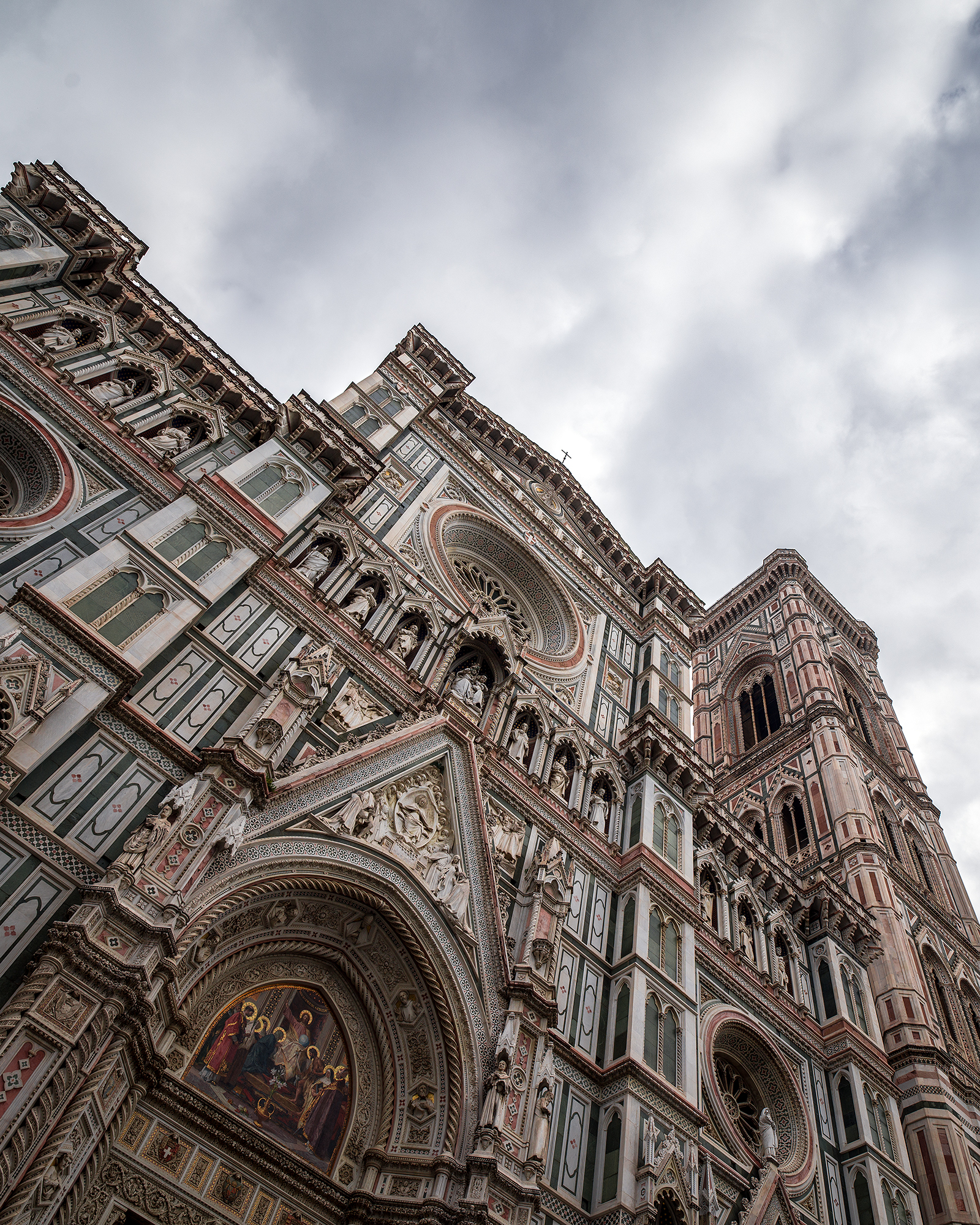 Cathedral of Santa Maria - A low-angle view captures an ornate cathedral facade and bell tower beneath a cloudy gray sky. - #FlorenceCathedral #SantaMariaDelFiore #DuomoDiFirenze #FlorenceDuomo #Duomo #Florence #Firenze #FlorenceItaly #Tuscany #Italy