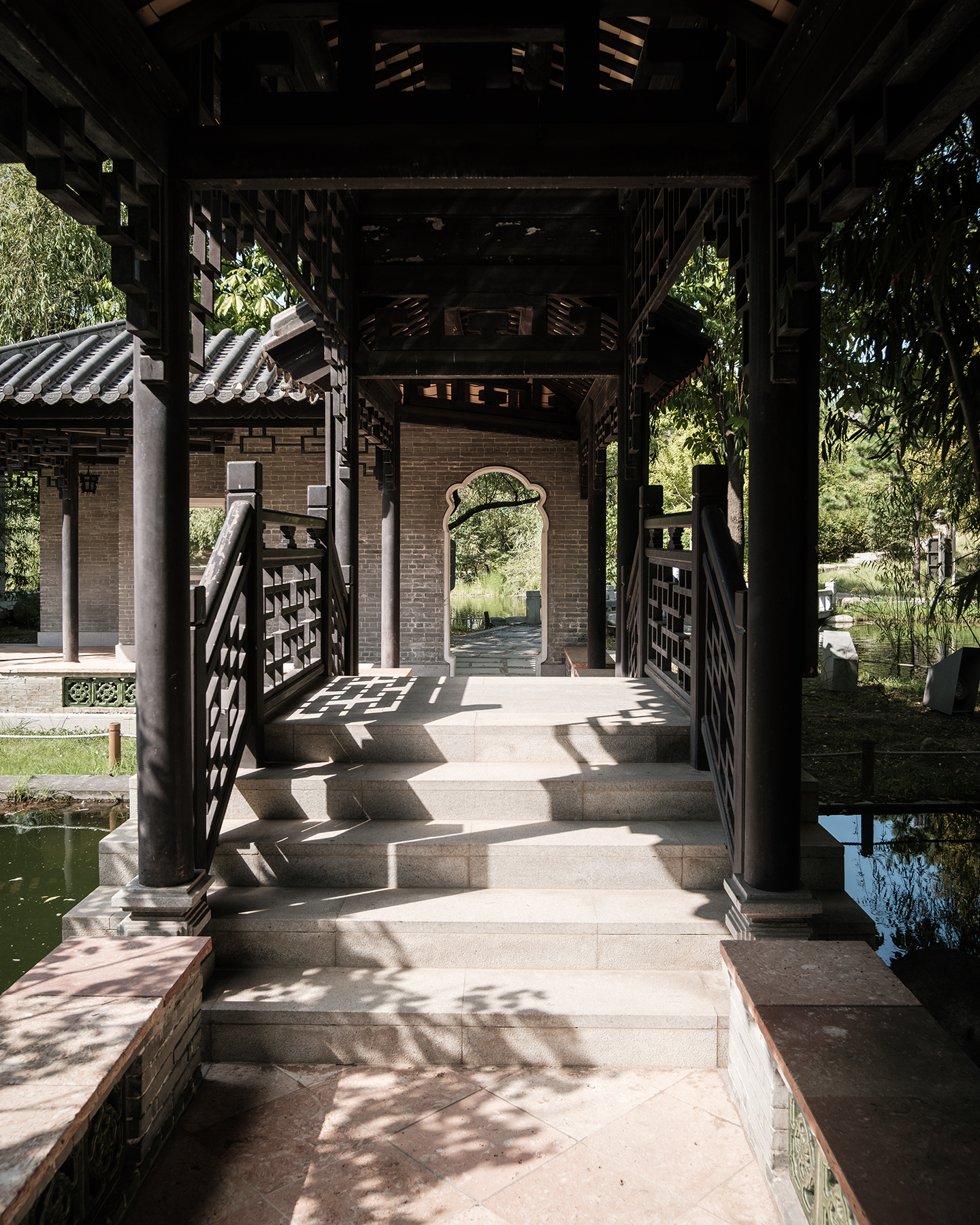 Wolhwawon - A shaded wooden garden pavilion frames stone steps, a tiled roof, and leafy pond reflections in dappled sunlight. - #Wolhwawon #WolhwawonGarden #Suwon #SuwonKorea #HyowonPark #GyeonggiDo #SouthKorea #KoreaTravel #VisitKorea #TravelKorea