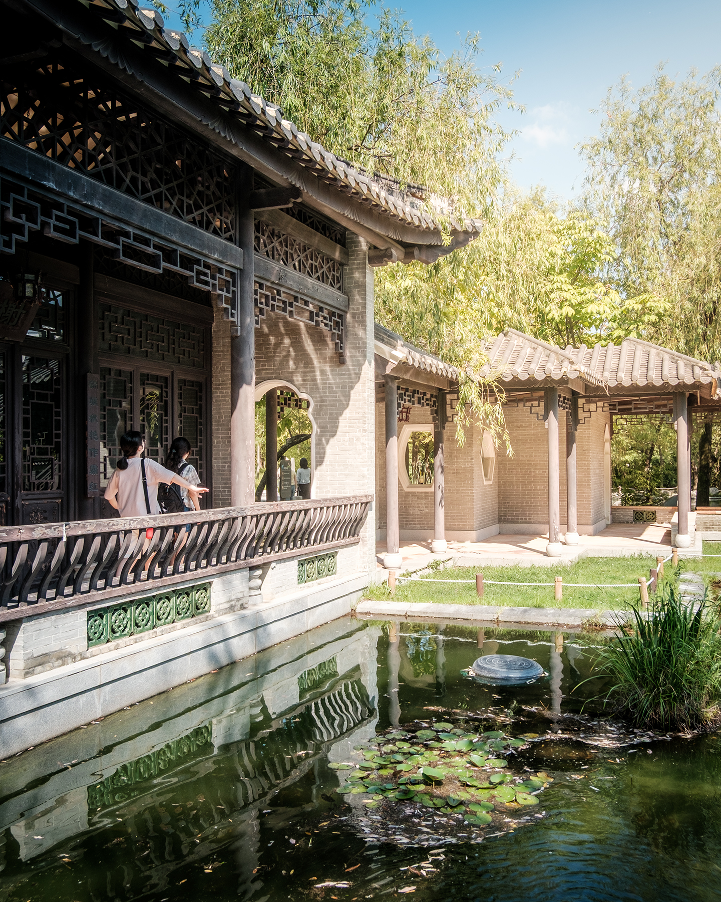 Wolhwawon - Sunlit traditional garden buildings with tiled roofs and lattice windows reflect in a pond beside lotus leaves. - #Wolhwawon #WolhwawonGarden #Suwon #SuwonKorea #HyowonPark #GyeonggiDo #SouthKorea #KoreaTravel #VisitKorea #TravelKorea