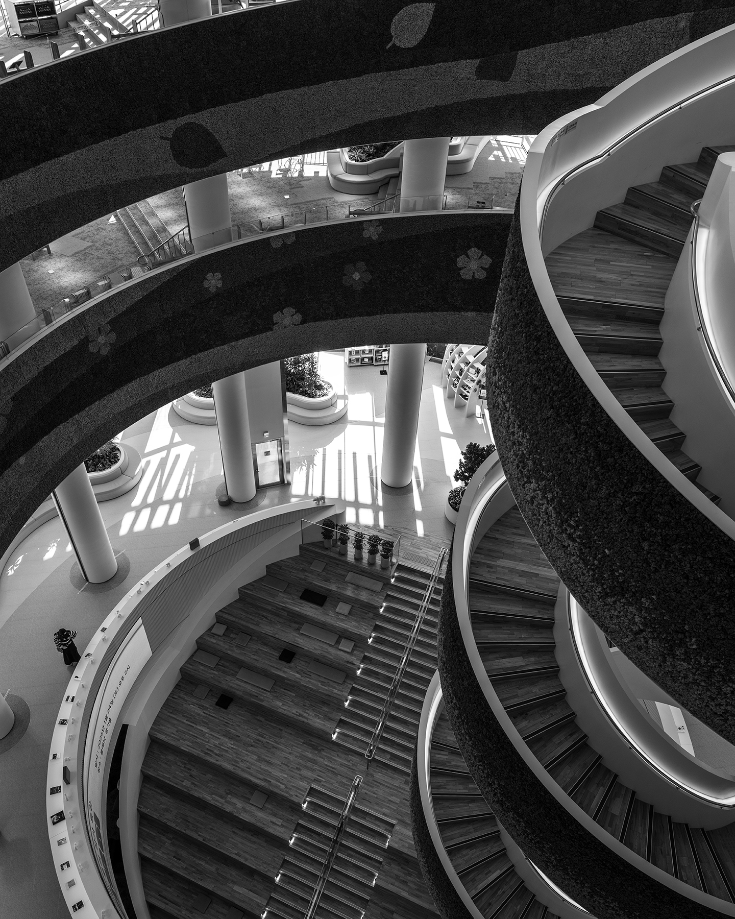 Gyeonggi Library - A black-and-white view looks down through sweeping library balconies, spiral stairs, columns, and sunlit floor patterns. - #GyeonggiLibrary #GyeonggiDo #Suwon #SuwonCity #Gwanggyo #Library #PublicLibrary #ModernLibrary #LibraryArchitecture #ArchitecturePhotography