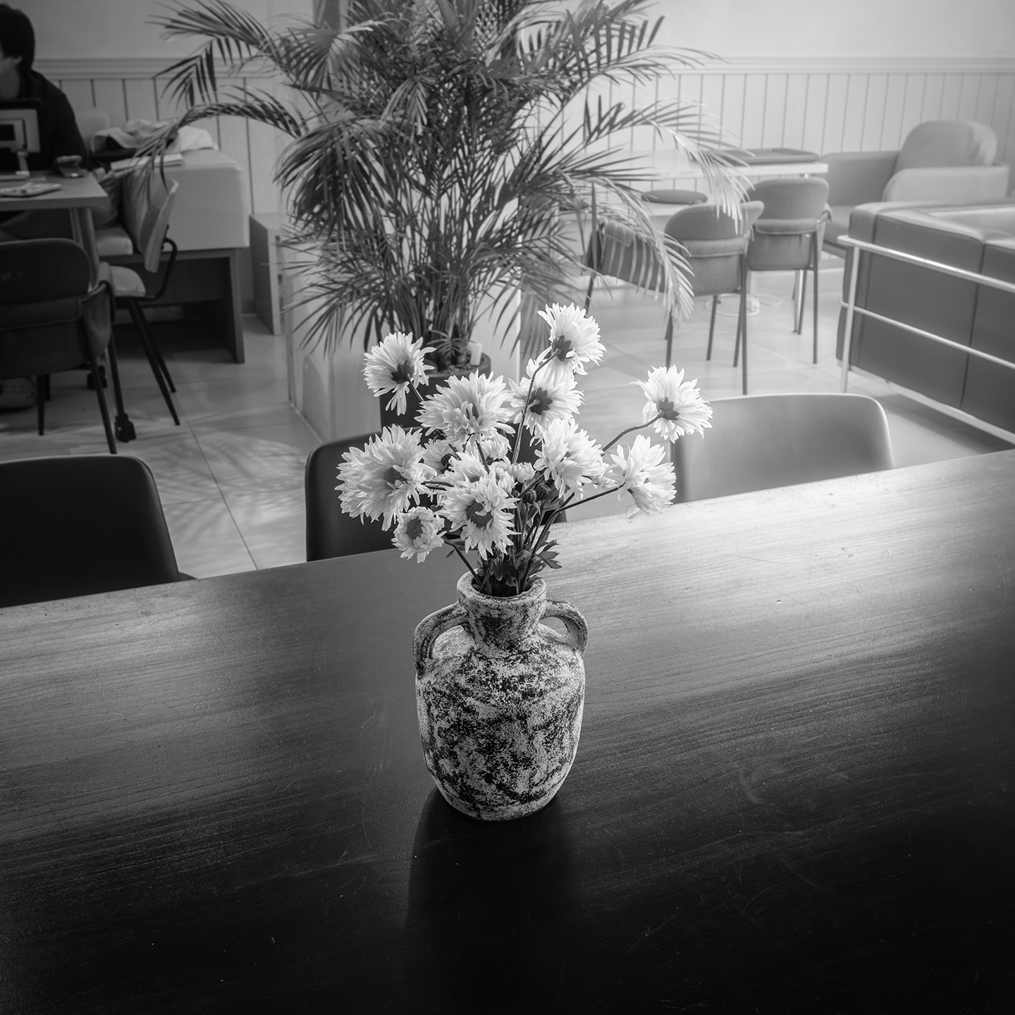 Flower - A black-and-white image shows a small vase of flowers on a dark table in a quiet indoor seating area. - #Cafe #Flower #Table #HouseYongam #SouthKorea
