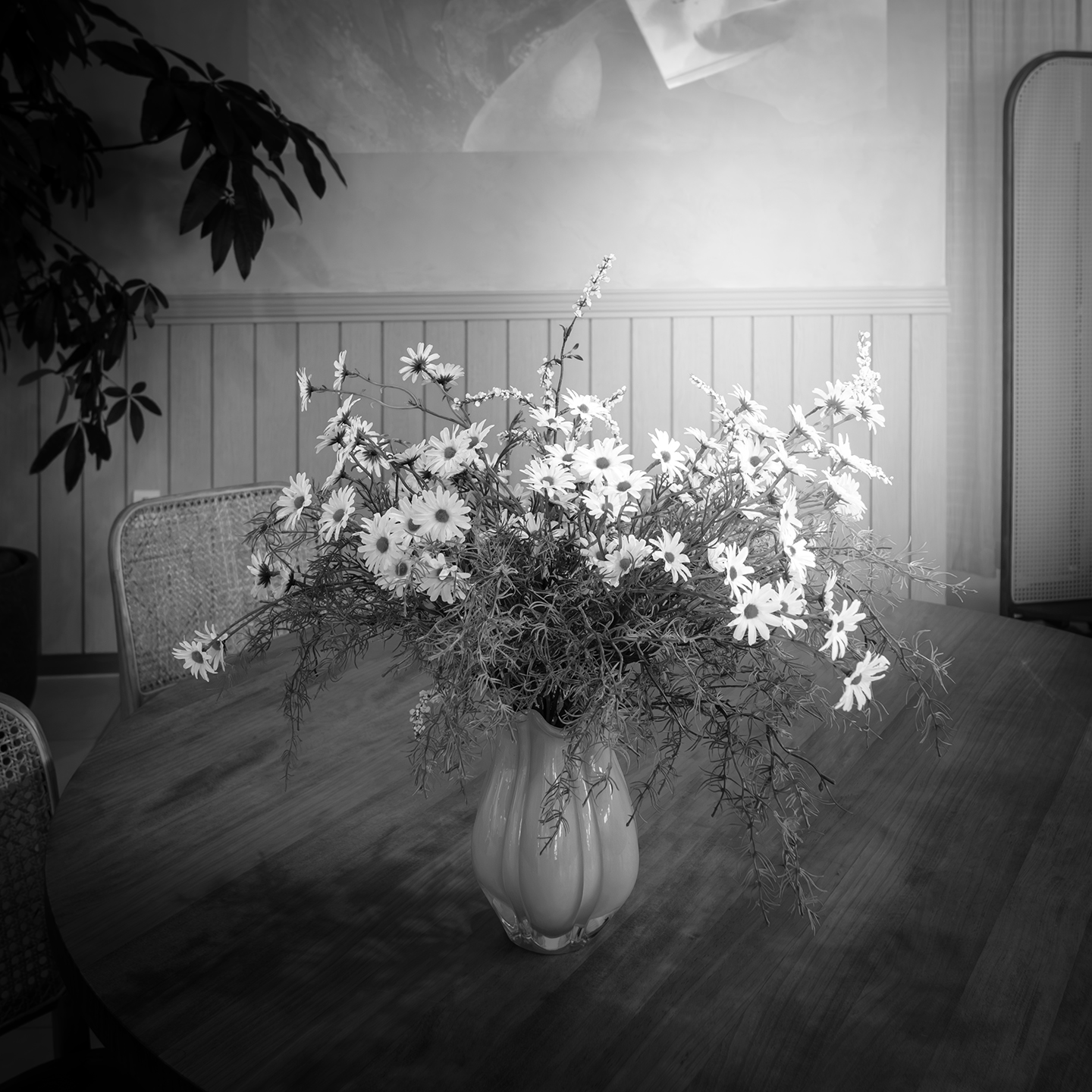 Flower - A black-and-white indoor still life shows a vase of daisies on a wooden table, lit softly beside chairs and paneled walls. - #Cafe #Flower #Table #HouseYongam #SouthKorea