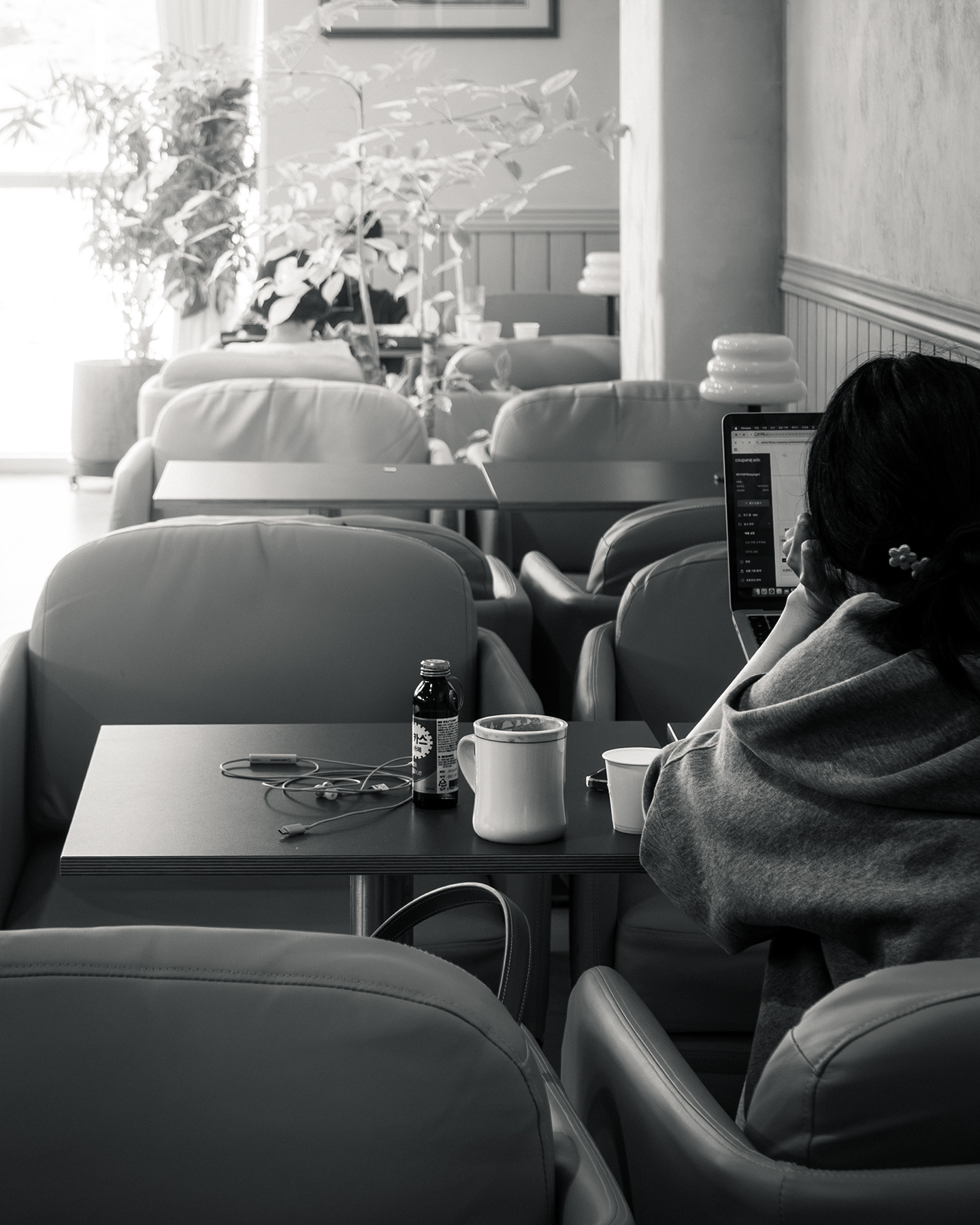 Study - A person studies on a laptop in a quiet cafe lounge, surrounded by armchairs, cups, and soft window light. - #Cafe #Study #Table #HouseYongam #SouthKorea