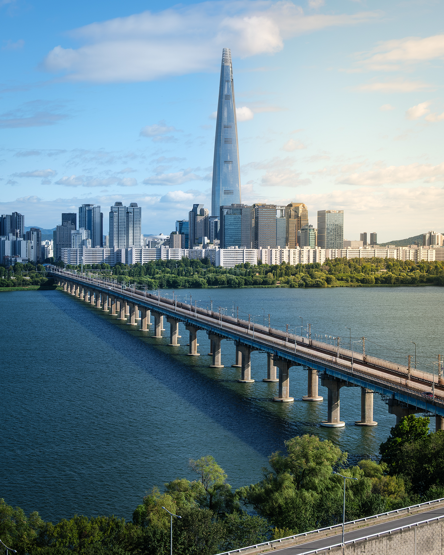 Han River - A long bridge crosses a broad river toward a dense skyline with a tall glass tower under soft afternoon clouds. - #HanRiver #Hangang #Seoul #SouthKorea #Korea #SeoulCity #SeoulLife #SeoulTravel #VisitSeoul #ExploreSeoul