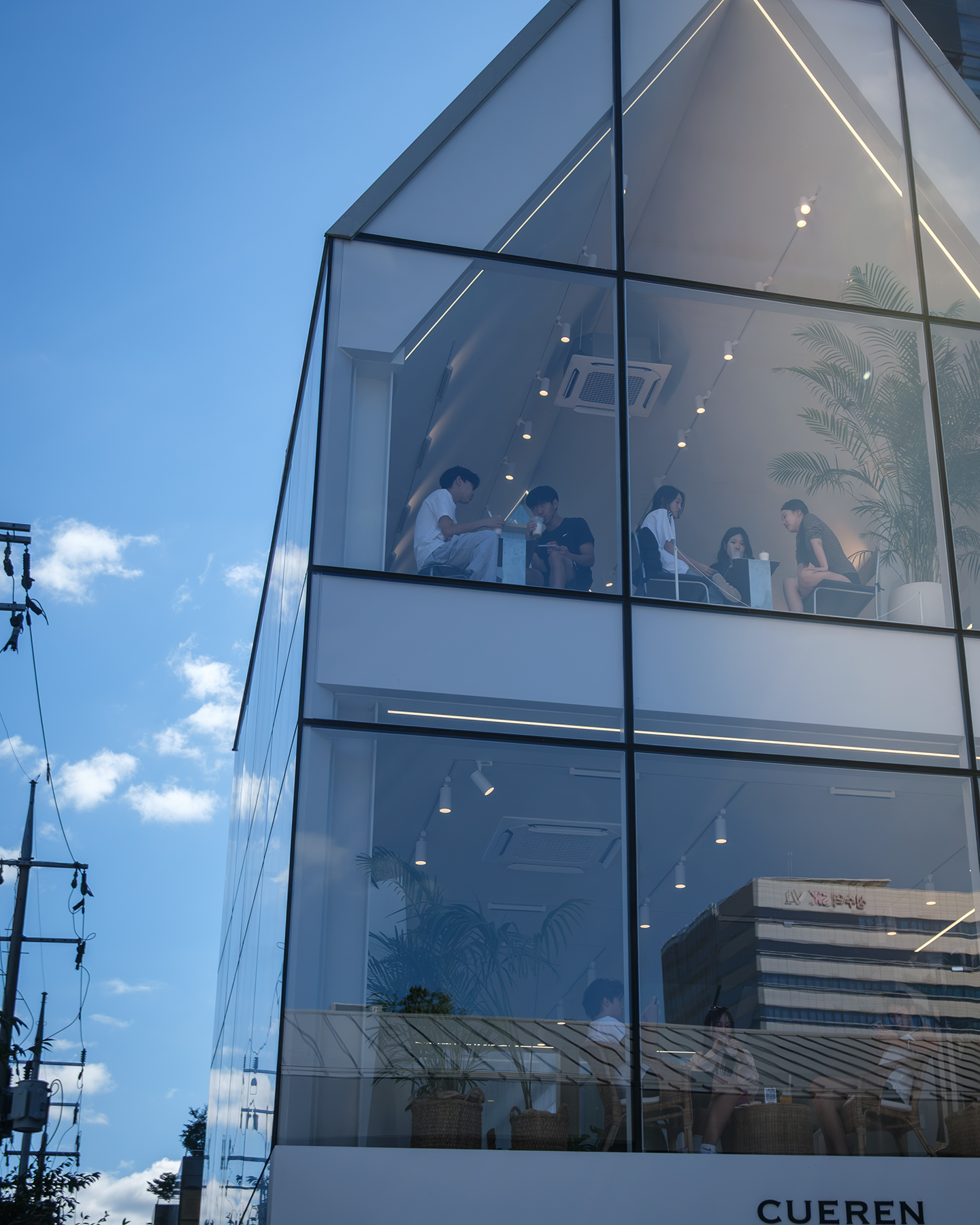 Cafe - People sit inside a modern glass-fronted cafe, framed by geometric windows, soft interior lights, reflections, and a clear blue sky. - #Cafe #SeongsuDong #Street #Seoul #SouthKorea