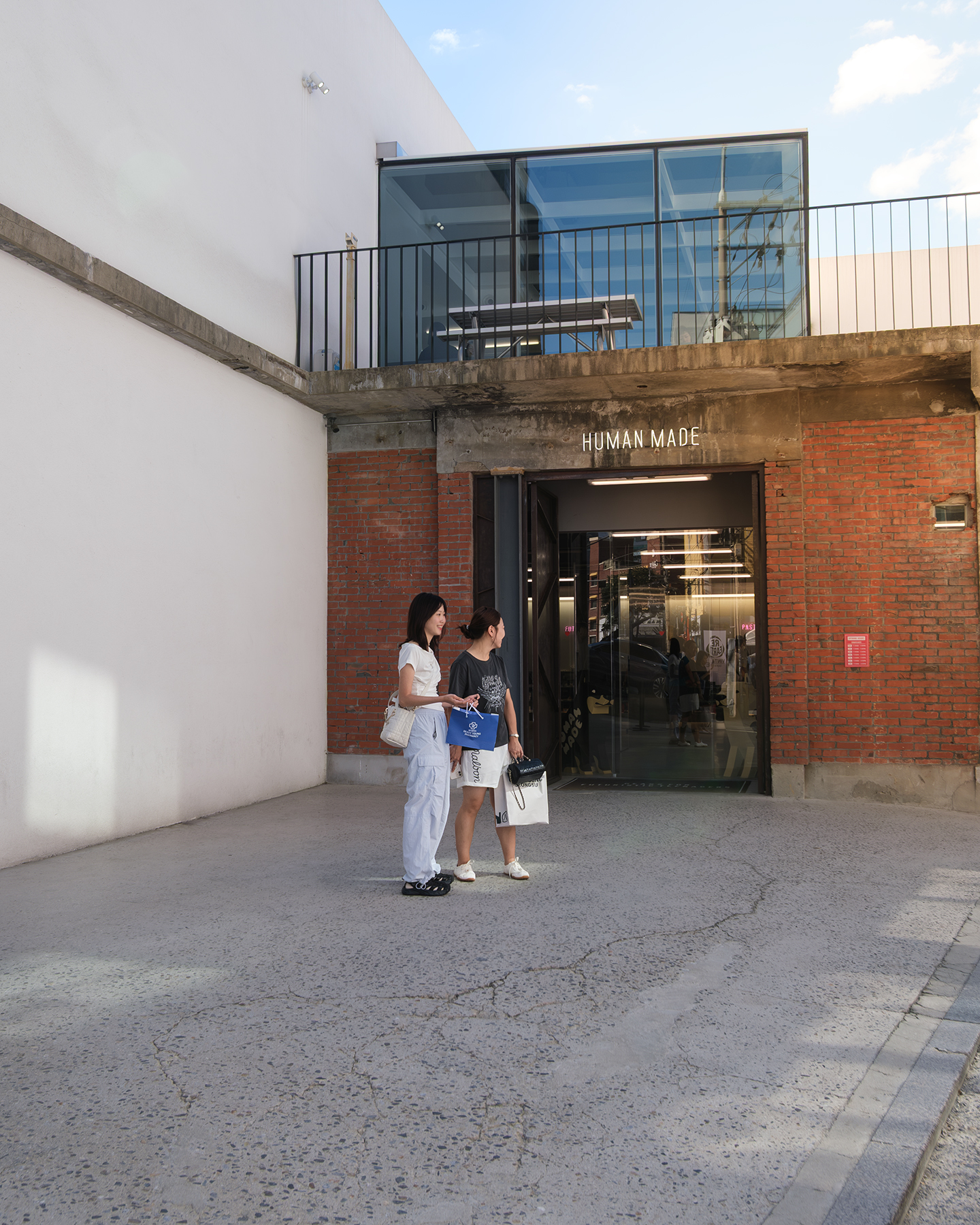 Store - Two shoppers stand outside a brick storefront with glass upper windows in bright afternoon light. - #Store #SeongsuDong #Street #Seoul #SouthKorea