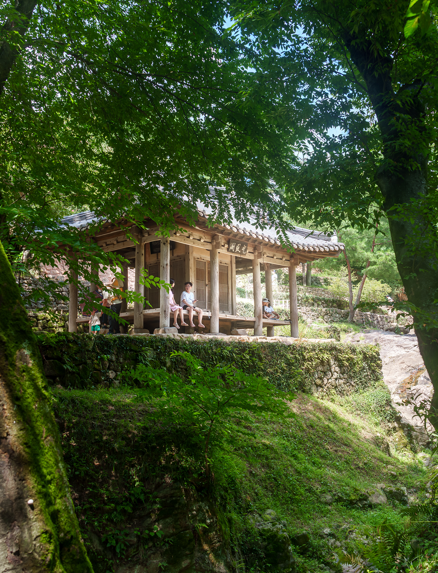 Soswaewon - A traditional wooden pavilion sits beneath dense green foliage, framed by stone walls and soft dappled light. - #Soswaewon #SoswaewonGarden #Damyang #DamyangTravel #KoreanGarden #TraditionalKoreanGarden #KoreanTraditionalGarden #HistoricGarden #GardenPhotography #NaturePhotography