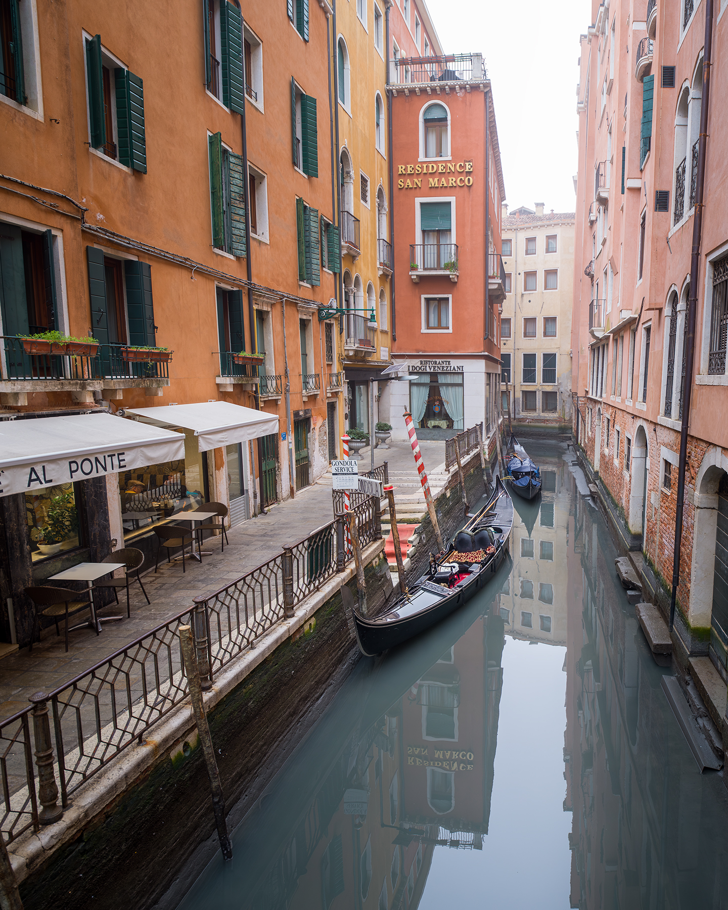 Venezia - Gondolas rest in a narrow canal between warm-toned buildings, with soft light and still water reflecting the façades. - #canal #gondola #architecture #urbanphotography #reflections #cityscape #travelphotography #historicbuildings #softlight #waterscape