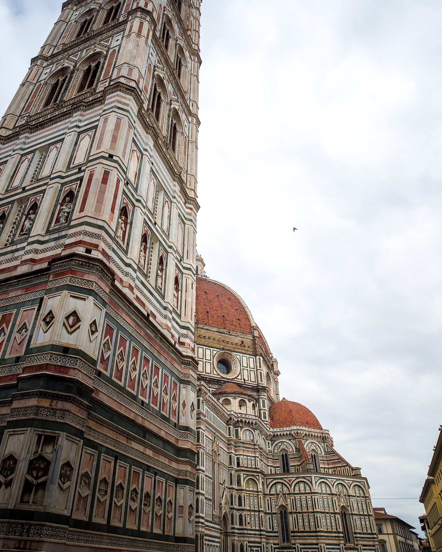 Cathedral of Santa Maria - An ornate cathedral tower and red-tiled domes rise against a cloudy sky in a dramatic low-angle architectural view. - #FlorenceCathedral #SantaMariaDelFiore #DuomoDiFirenze #FlorenceDuomo #Duomo #Florence #Firenze #FlorenceItaly #Tuscany #Italy