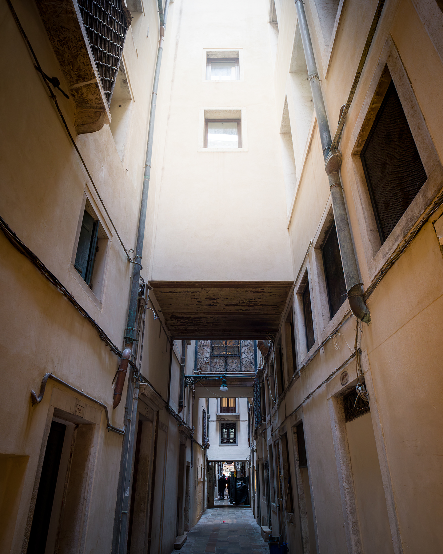 Alley - A narrow alley rises between pale building walls, with pipes, windows, and overhead walkways leading toward soft daylight. - #Venice #Venezia #VeniceItaly #VeniceStreets #VeniceAlley #VeniceAlleys #VenetianStreets #VenetianAlley #HiddenVenice #SecretVenice