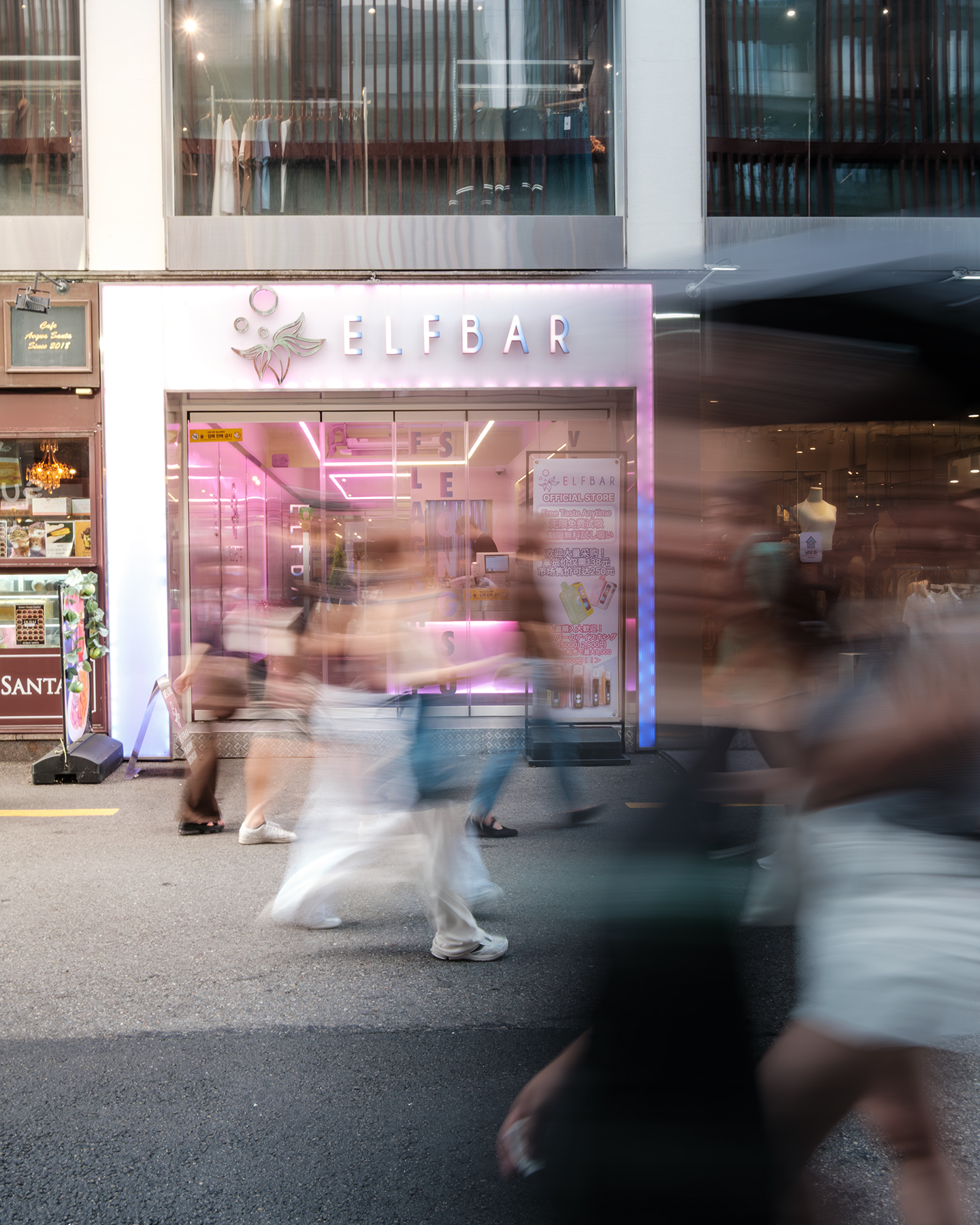 Passerby - Blurred pedestrians pass a pink-lit storefront, creating a layered street scene of motion and urban light. - #Pedestrian #Passerby #StreetLife #PeopleOnTheStreet #StreetPhotography #UrbanLife #CityLife #StreetScene