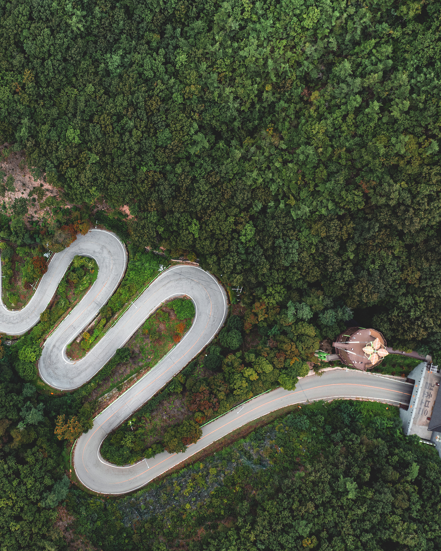 Maltijae - An aerial view shows a winding mountain road cutting through dense green forest in soft, overcast light. - #Maltijae #MaltijaePass #Boeun #Chungcheongbukdo #SouthKorea #KoreaTravel #KoreaLandscape #KoreaScenery #MountainRoad #ScenicRoad
