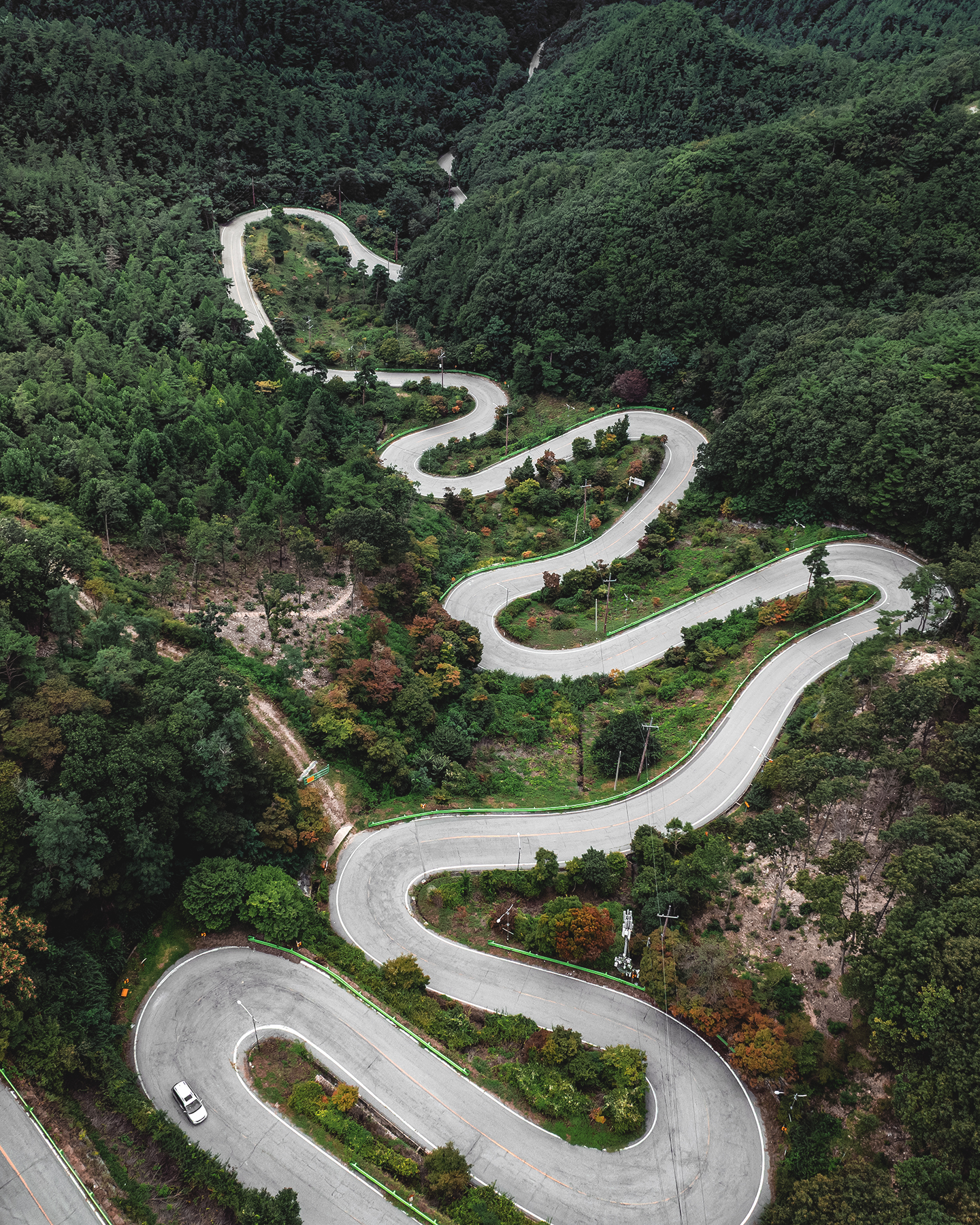 Maltijae - An aerial view shows a winding mountain road cutting through dense green forest under soft, muted light. - #Maltijae #MaltijaePass #Boeun #Chungcheongbukdo #SouthKorea #KoreaTravel #KoreaLandscape #KoreaScenery #MountainRoad #ScenicRoad