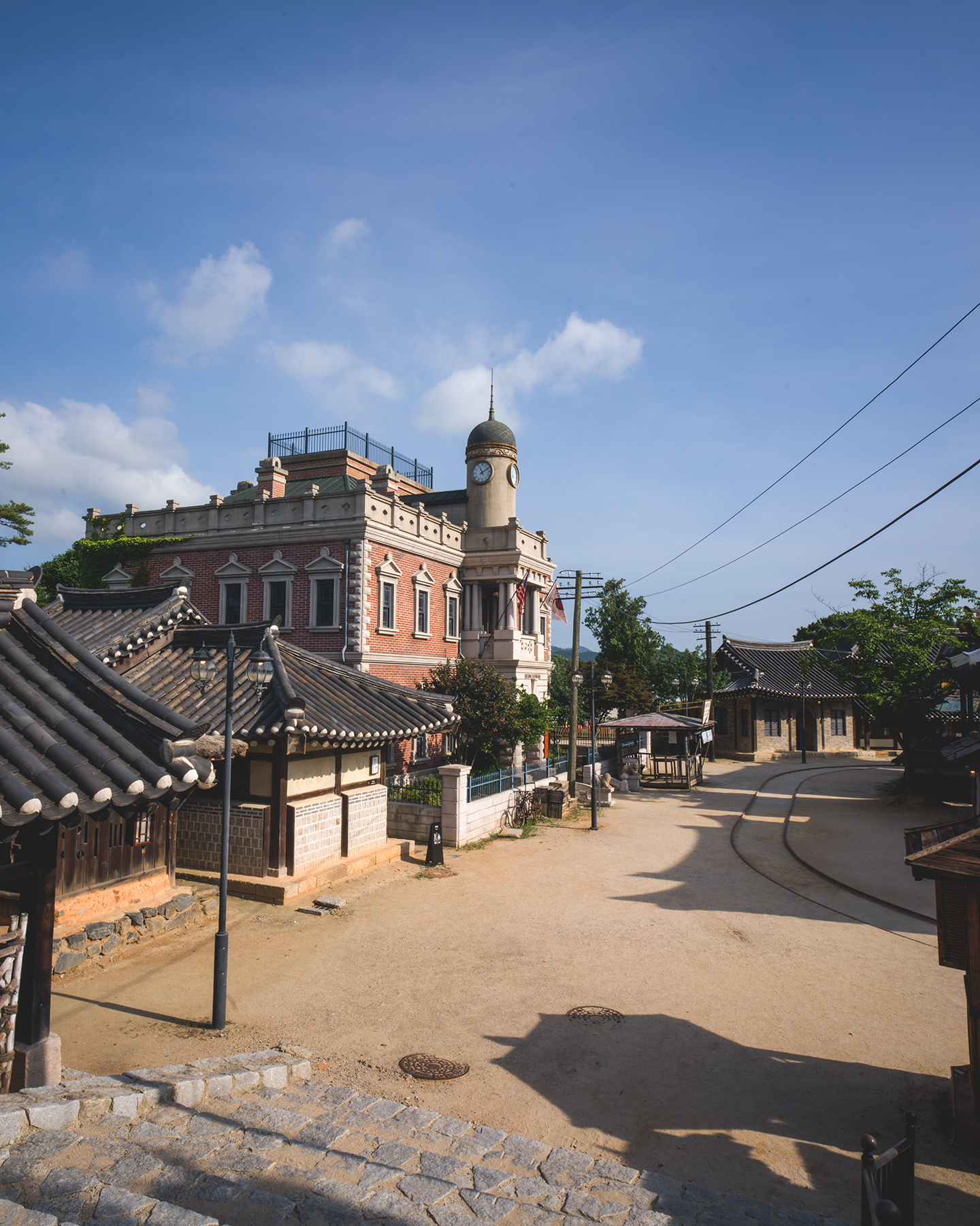 Sunshine Studio - Sunlit traditional tiled roofs and a red brick clock tower frame a quiet historic street under a clear blue sky. - #SunshineStudio #NonsanSunshineStudio #Nonsan #Chungcheongnamdo #SouthKorea #KoreaTravel #KoreaPhotography #TravelPhotography #DramaFilmingLocation #KDramaLocation