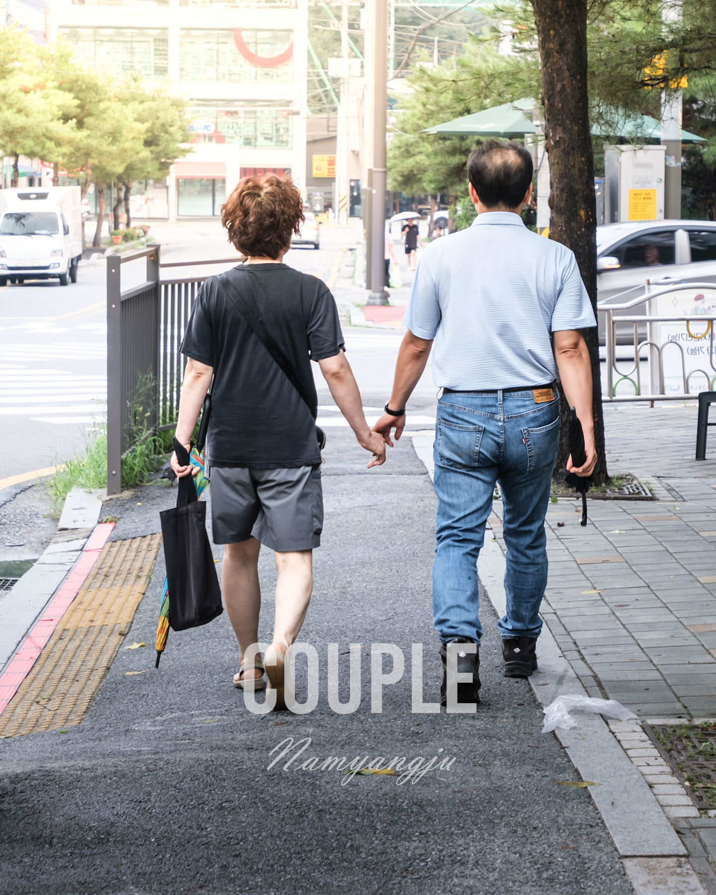 Couple - A couple walks hand in hand along a tree-lined city sidewalk in soft daylight, photographed from behind. - #StreetCouple #Couple #CouplePhotography #StreetPhotography #StreetLife #UrbanLife #CityLife #CityStreets #StreetScene #CandidPhotography