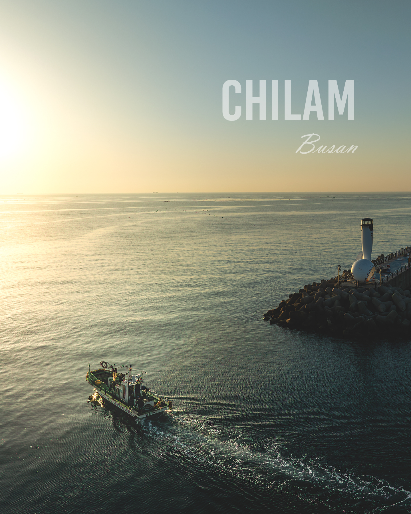 Chilam - A small boat leaves a foamy wake across calm golden water near a breakwater lighthouse under a hazy sky. - #ChilamPort #ChilamHarbor #Gijang #Busan #FishingBoat #KoreanFishingBoat #FishingVillage #CoastalVillage #KoreanCoast #SeaScape