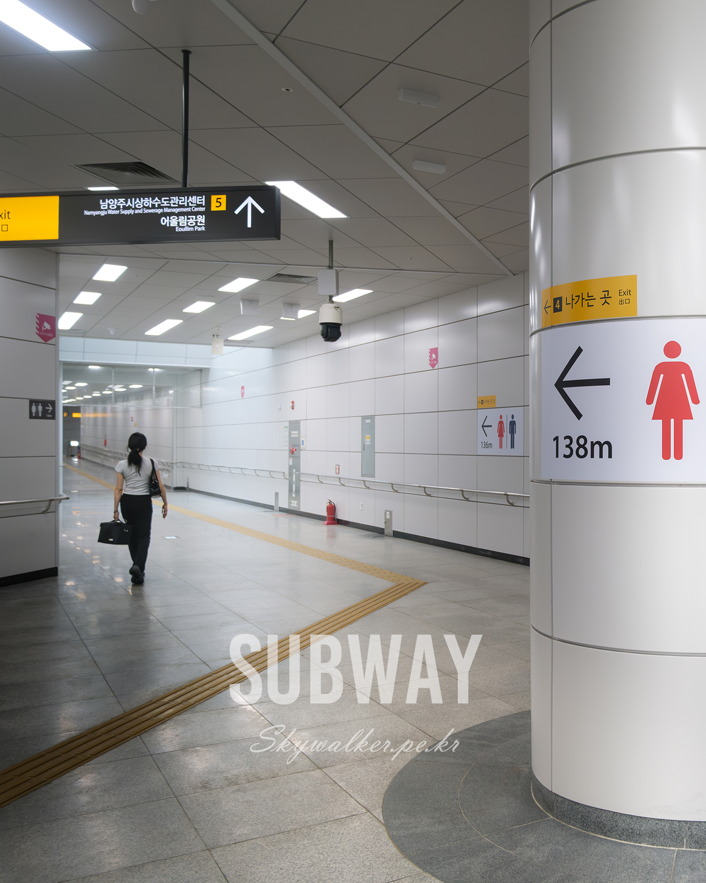 Subway - A lone commuter walks through a brightly lit subway corridor with exit signs, tiled walls, and yellow tactile paving. - #SubwayRestroom #SubwayToilet #MetroRestroom #MetroToilet #PublicRestroom #PublicToilet #SubwayStation #MetroStation #UndergroundStation #UrbanLife