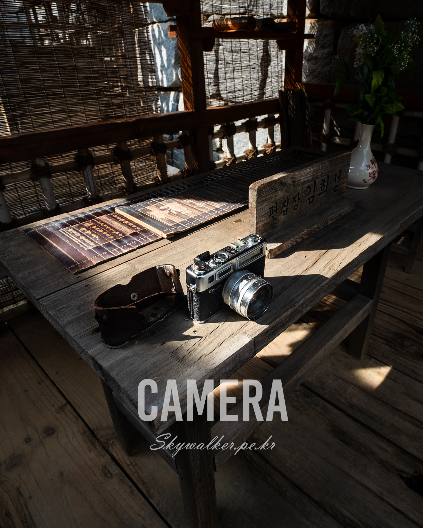 Camera - A vintage camera rests on a wooden table in warm slatted sunlight, surrounded by papers, shadows, and rustic decor. - #VintageCamera #ClassicCamera #FilmCamera #RangefinderCamera #RetroCamera #CameraLovers #CameraPhotography #PhotographyGear #VintagePhotography #BlackAndWhite