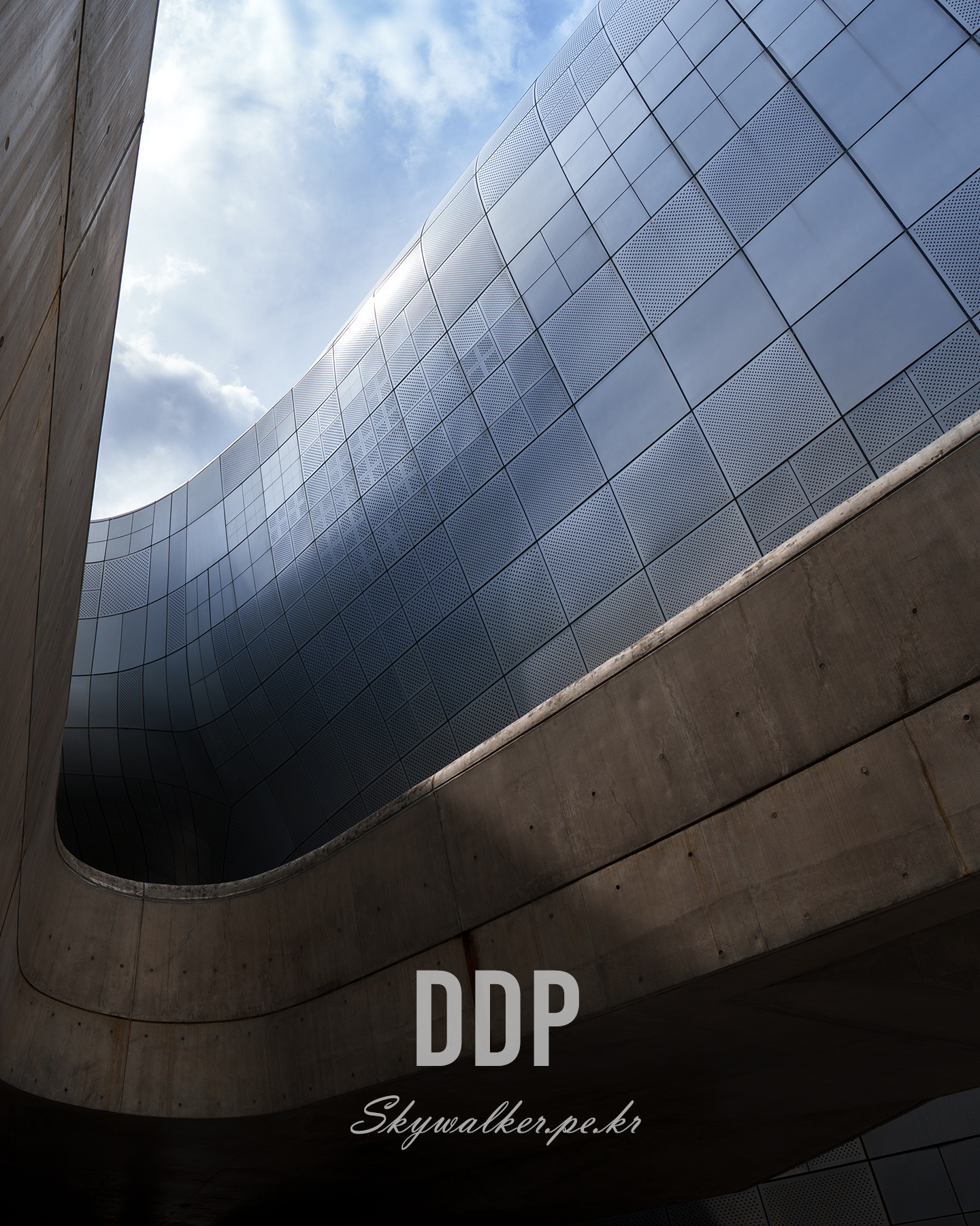 DDP - Curving metal panels and concrete walls frame a bright sky in an upward view of modern architecture. - #Architecture #ModernArchitecture #UrbanDesign #MetalFacade #Concrete #Curves #Sky #Sunlight #Geometry #Minimalism