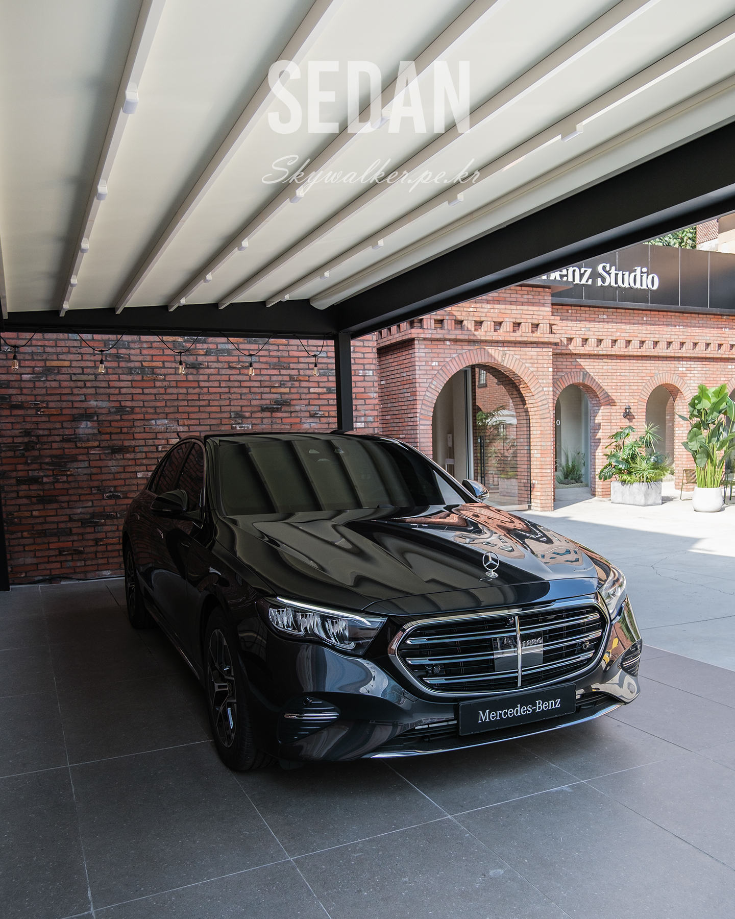 Sedan - A black Mercedes-Benz sedan sits under a modern canopy beside brick arches, with soft daylight reflecting on its glossy hood. - #sedan #mercedesbenz #blackcar #luxurycar #carphotography #covereddriveway #brickarchitecture #urbanstyle #daylight #automotive