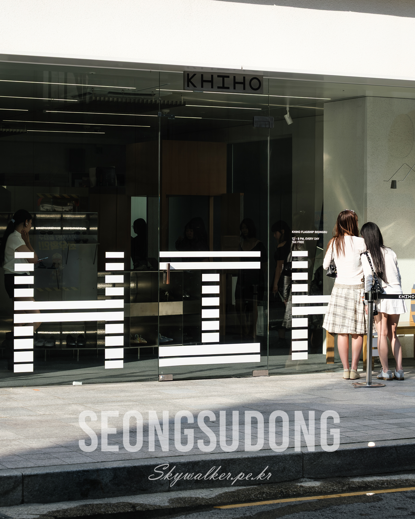 Seongsudong - Two women stand by a glass storefront with bold white graphics, reflected interiors, and sharp afternoon sunlight. - #Seongsudong #StreetPhotography #Storefront #GlassFacade #UrbanScene #WindowGraphics #Sunlight #Reflections #MinimalDesign #CityWalk