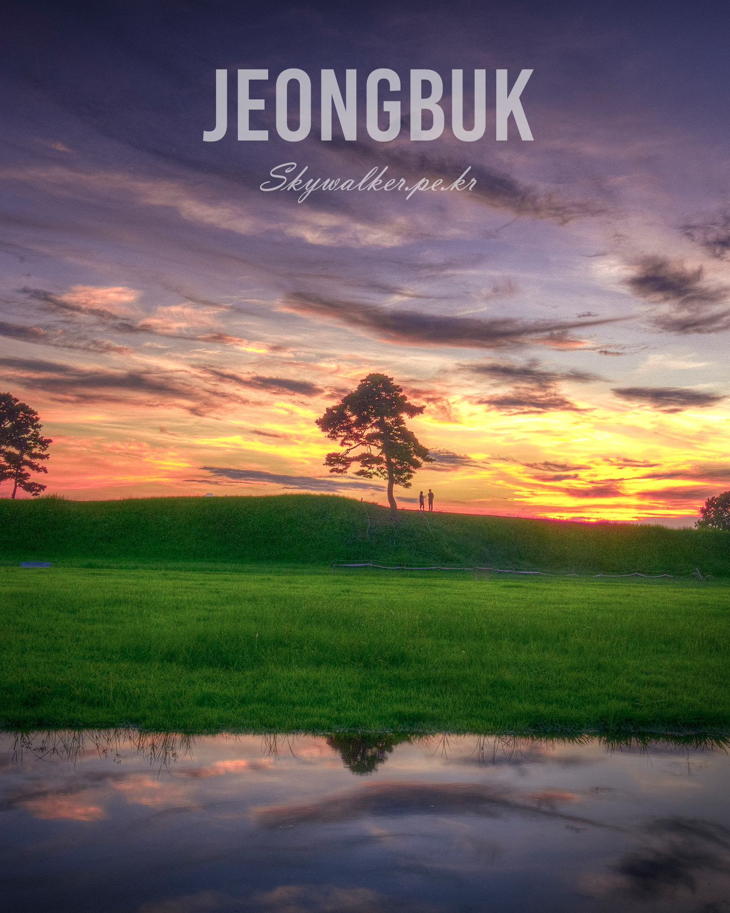 Jeongbuk Fortress - A lone tree and two small silhouetted figures stand on a grassy ridge beneath a vivid sunset sky reflected in still water. - #SunsetLandscape #LoneTree #Silhouette #GoldenHour #Cloudscape #Reflection #Grassland #EveningSky #NaturePhotography #SereneMood