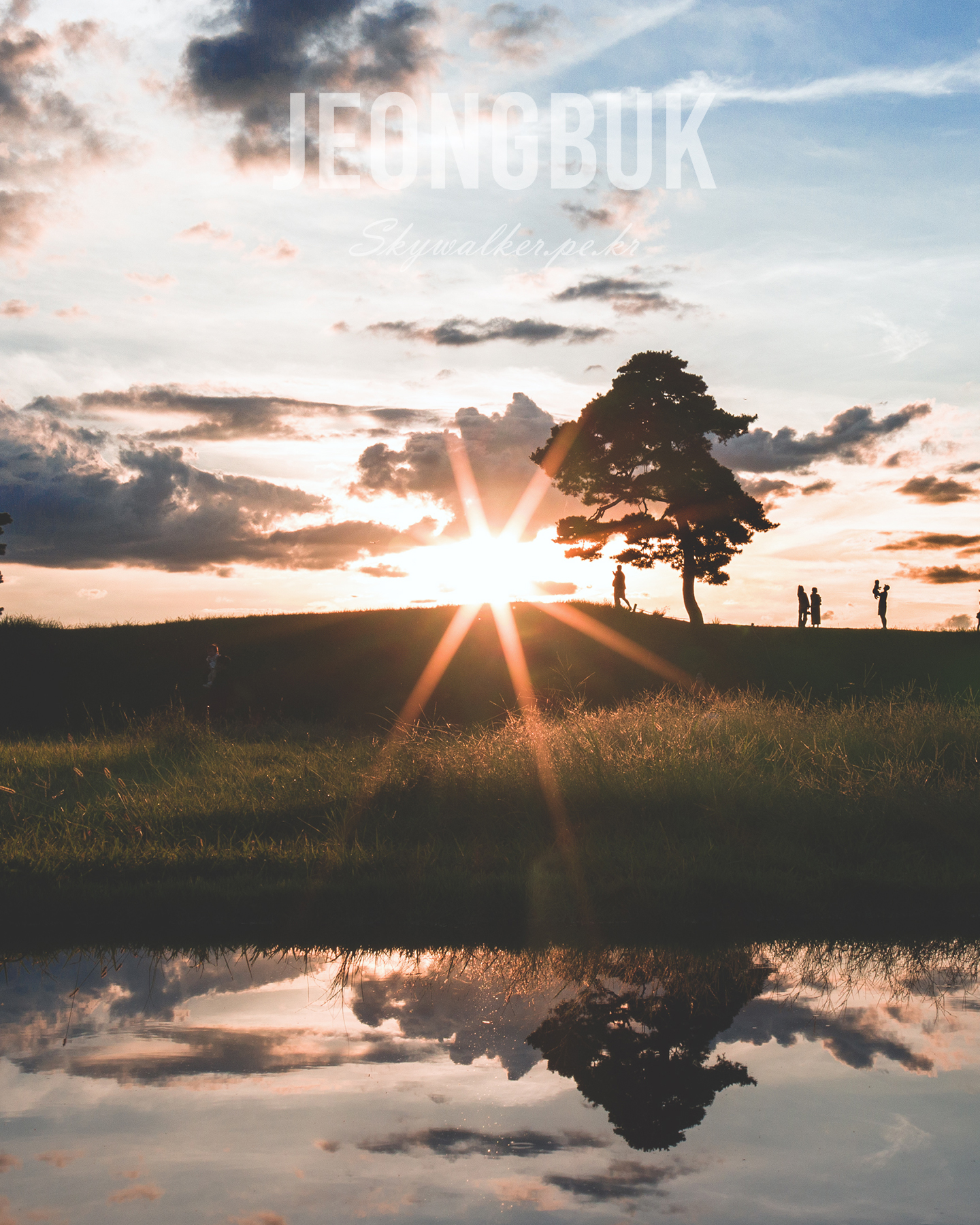 Jeongbuk Fortress - Silhouetted figures and a lone tree stand on a grassy ridge as a low sun and clouds reflect in still water. - #sunset #silhouette #tree #reflection #clouds #landscape #goldenhour #waterscape #grassland #backlight