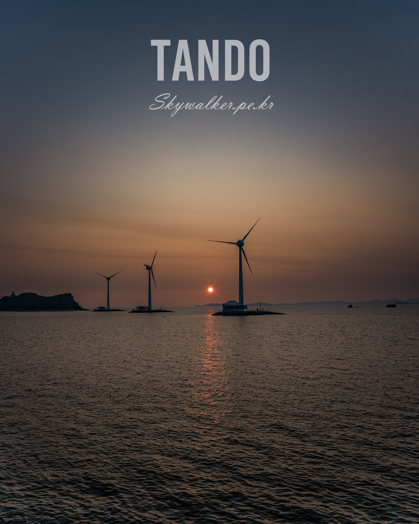 Tando - Three offshore wind turbines stand in calm water at sunset, silhouetted against a hazy orange sky and reflected light. - #OffshoreWind #WindTurbines #Sunset #Seascape #GoldenHour #Silhouette #RenewableEnergy #OceanView #HazySky #Reflection
